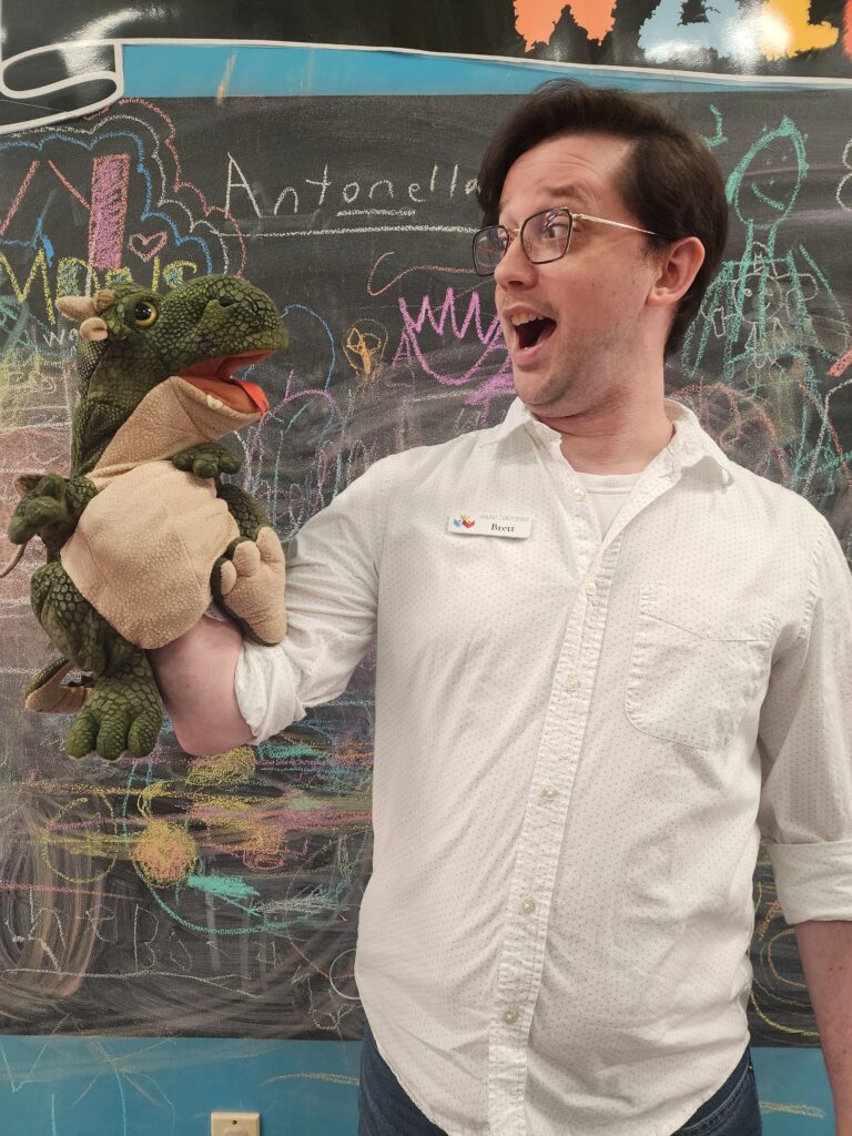 Teen Librarian, Brett, shows a dinosaur puppet.
