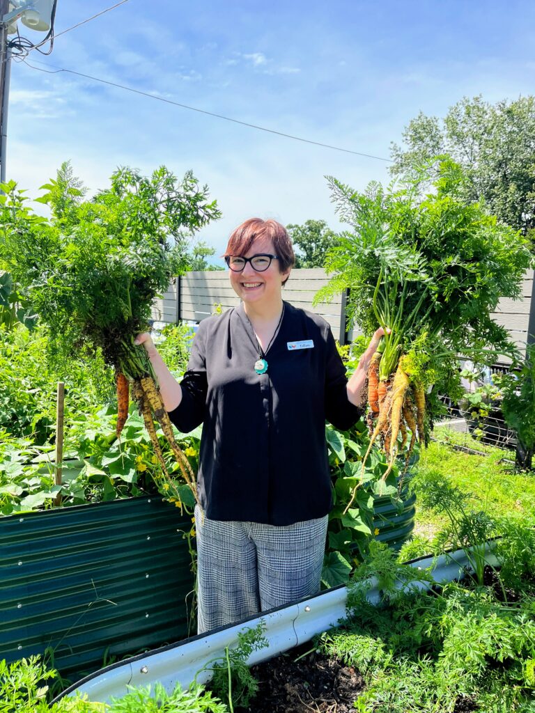 Person smiles as they hold up carrots harvested from raised beds.