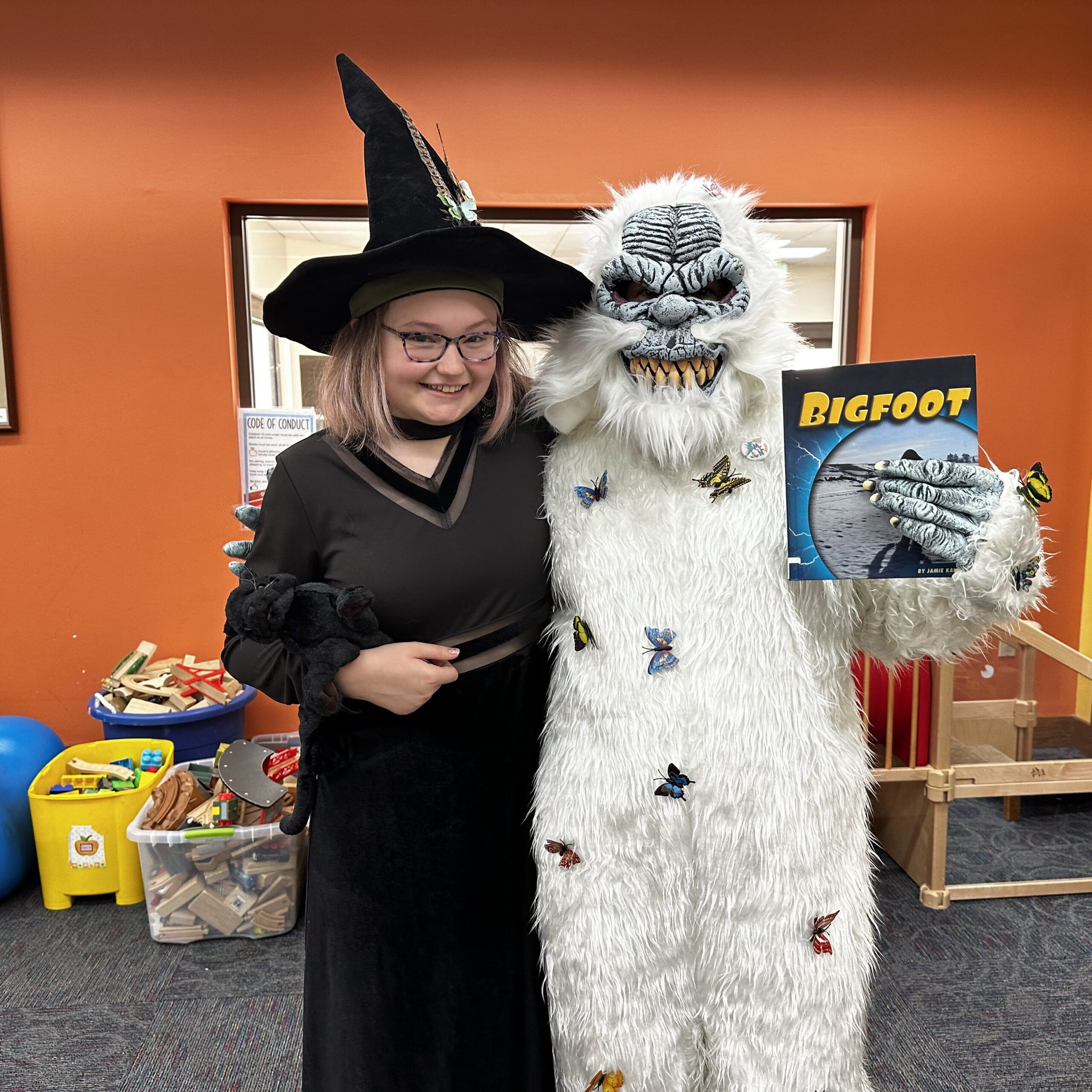 Young patron dressed as a witch poses with a yeti holding a Bigfoot book.