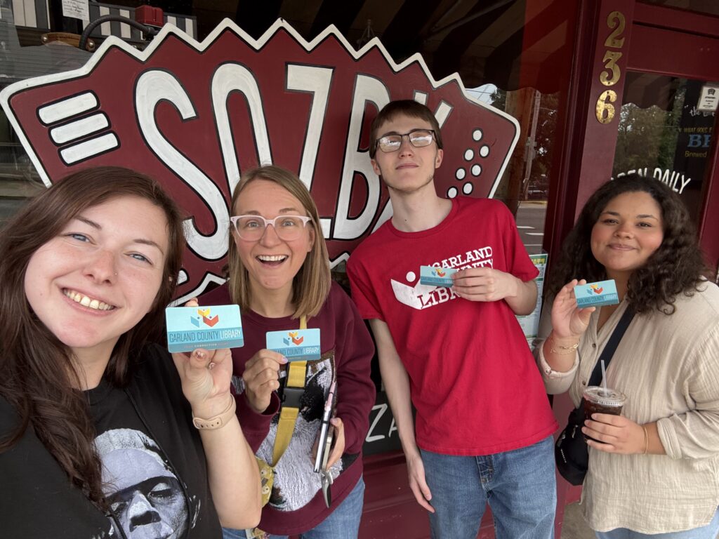 Library staff holding their library cards in front of SQZBX Pizza