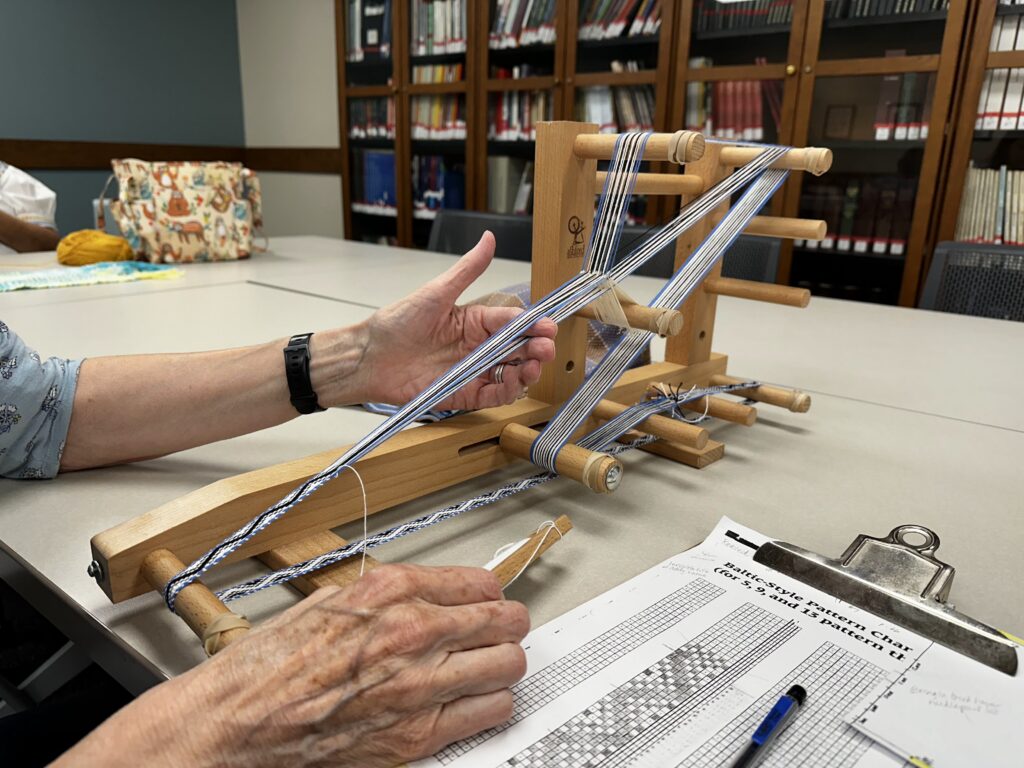 A person demonstrates weaving on a loom at a library program.