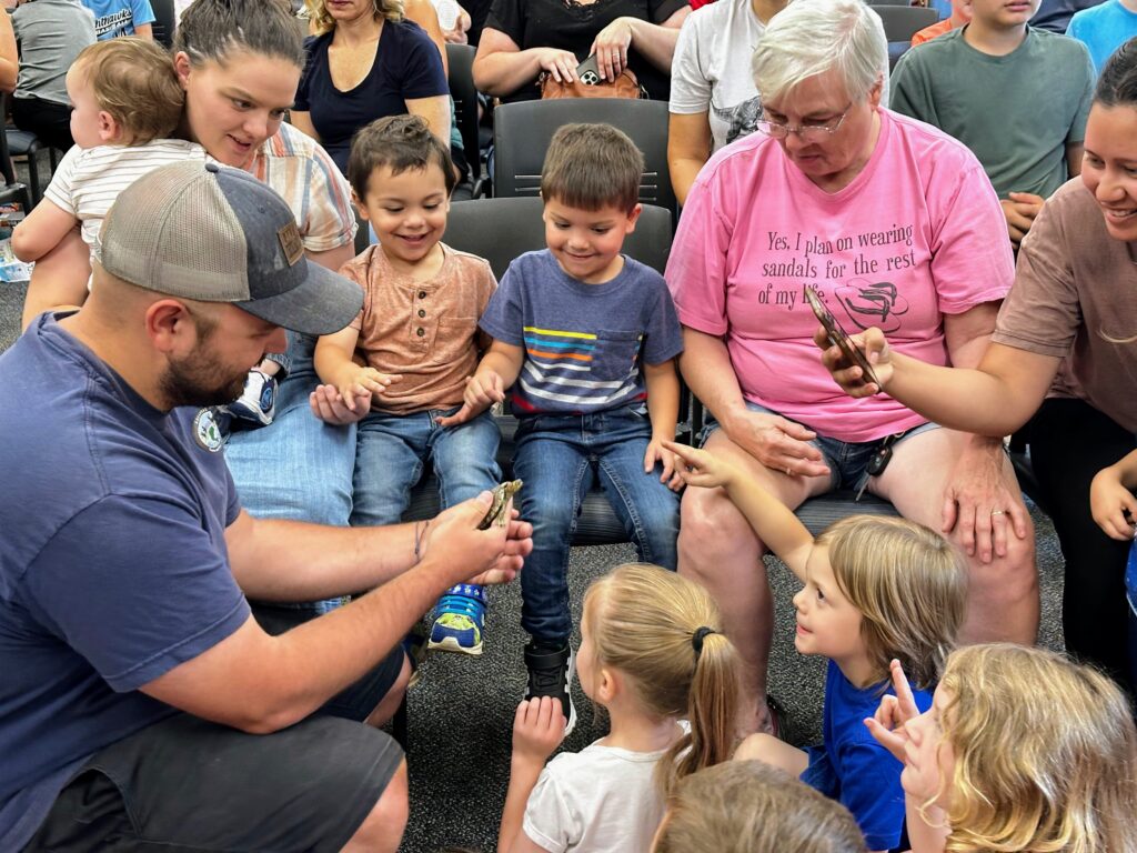 Patrons gather around a person holding a turtle for an animal program.