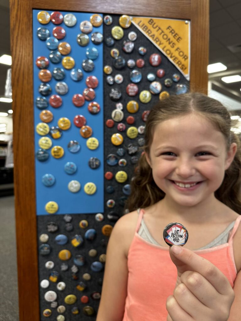 Young patron smiles while holding a library button.