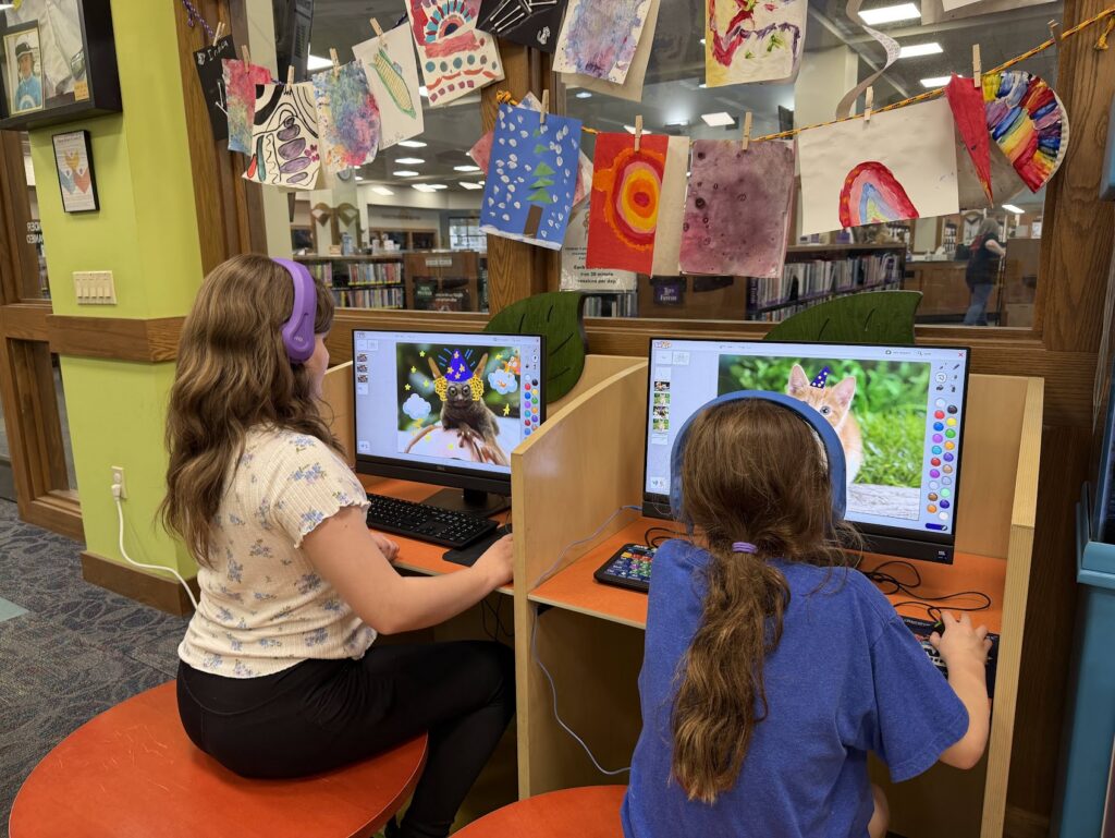 Two children wearing headphones while playing on computers in the Children's Library.