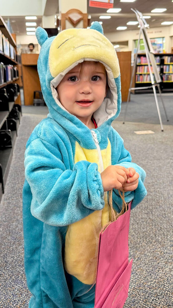 Child in a costume holding a pink bag at the Library.