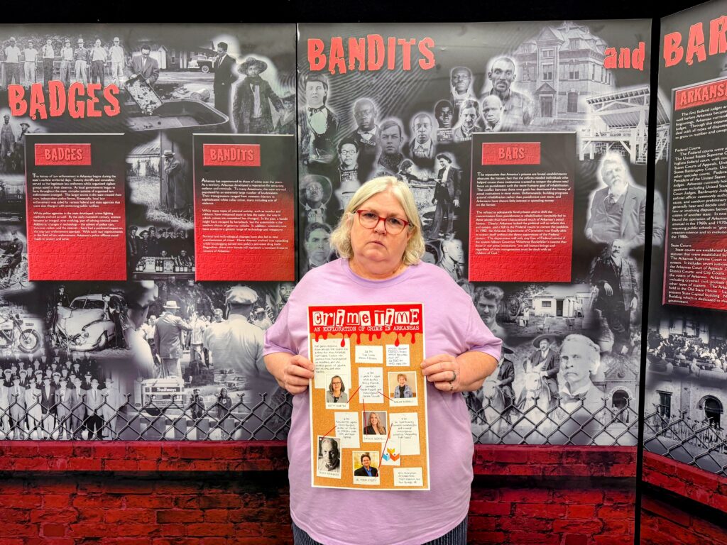 Staff member poses in front of traveling display featuring true crime information.