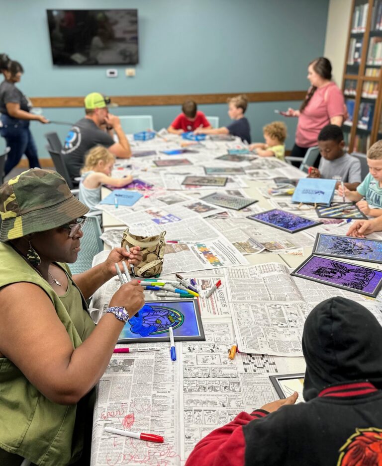 group of children and adults coloring with markets on what looks like stained glass